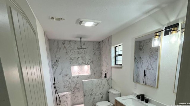 bathroom featuring vanity, tiled shower, and toilet