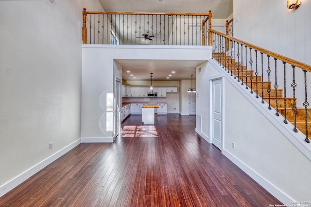 unfurnished living room with ceiling fan, dark hardwood / wood-style flooring, and a high ceiling