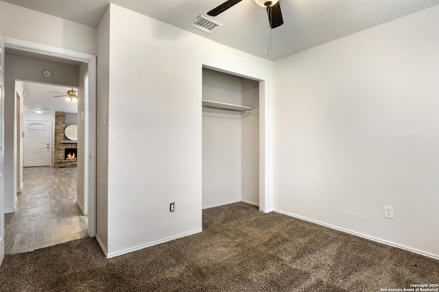 unfurnished bedroom featuring dark carpet, a closet, a brick fireplace, and ceiling fan