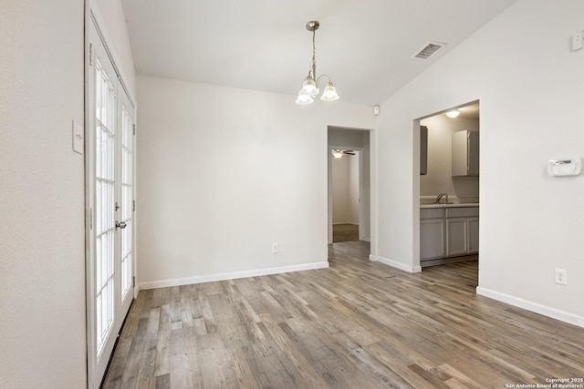 spare room featuring sink, french doors, light hardwood / wood-style flooring, a chandelier, and vaulted ceiling