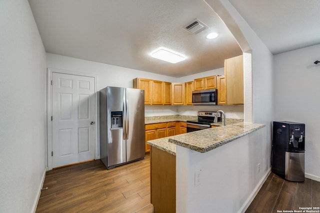 kitchen featuring kitchen peninsula, a textured ceiling, stainless steel appliances, and light stone counters