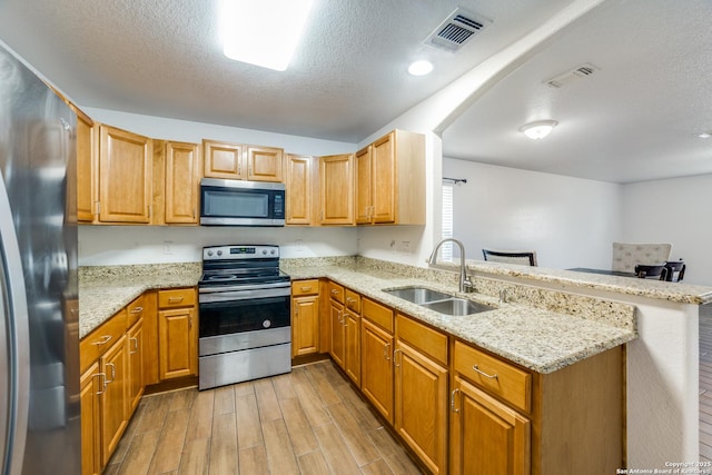 kitchen with kitchen peninsula, light stone counters, a textured ceiling, stainless steel appliances, and sink