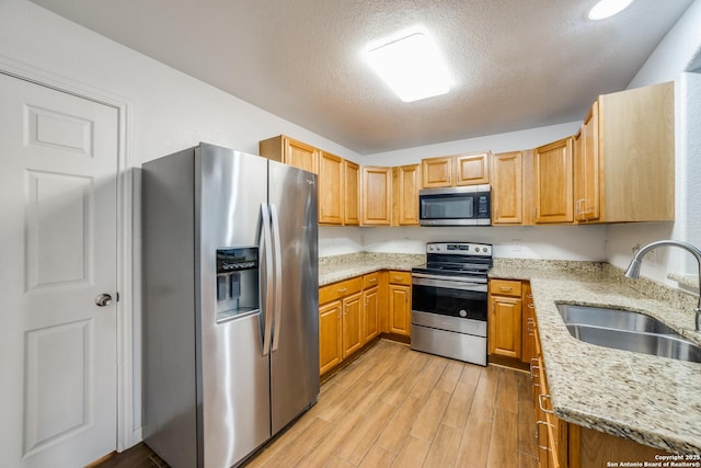 kitchen featuring light stone counters, a textured ceiling, stainless steel appliances, sink, and light hardwood / wood-style floors