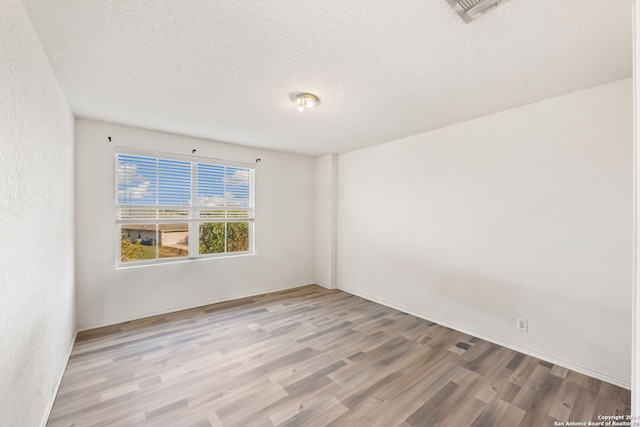 empty room with a textured ceiling and light hardwood / wood-style flooring