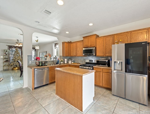 kitchen with ceiling fan, sink, hanging light fixtures, kitchen peninsula, and appliances with stainless steel finishes