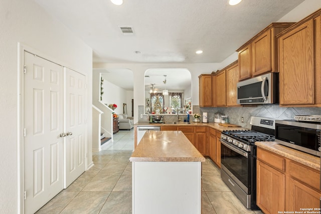 kitchen with ceiling fan, a center island, stainless steel appliances, backsplash, and light tile patterned floors