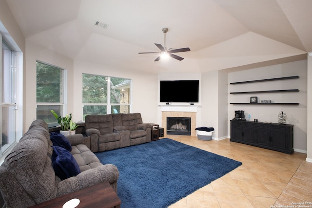 tiled living room with vaulted ceiling, a raised ceiling, ceiling fan, and a tiled fireplace