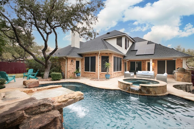 rear view of property featuring pool water feature, a swimming pool with hot tub, an outdoor kitchen, and solar panels