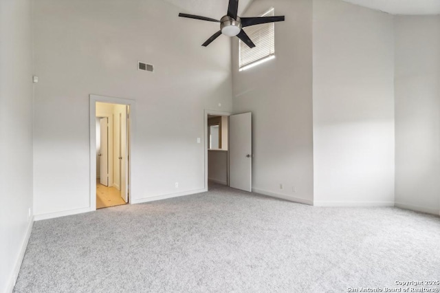 carpeted spare room featuring ceiling fan and a towering ceiling