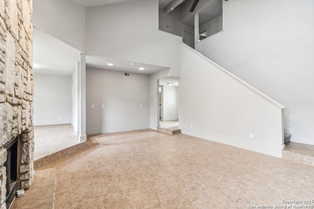 unfurnished living room with tile patterned floors, a stone fireplace, and a high ceiling