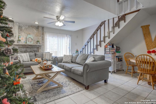 tiled living room featuring ceiling fan, a fireplace, and a textured ceiling