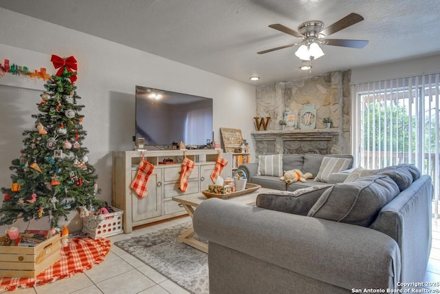 living room featuring ceiling fan, a fireplace, light tile patterned floors, and a textured ceiling