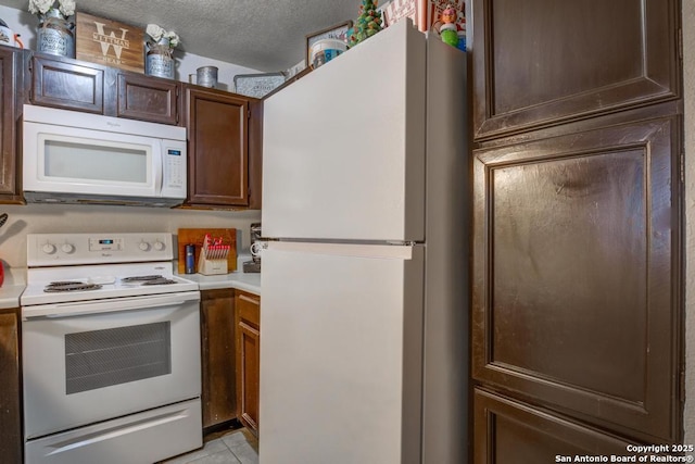 kitchen featuring a textured ceiling, white appliances, light tile patterned floors, and dark brown cabinetry