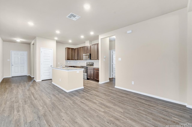 kitchen featuring appliances with stainless steel finishes, backsplash, sink, hardwood / wood-style flooring, and an island with sink