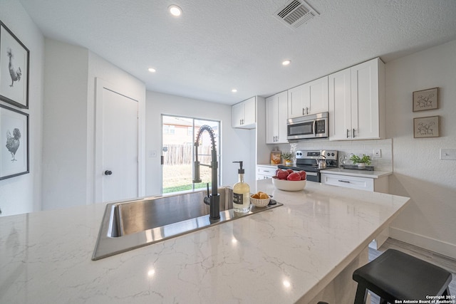 kitchen with sink, light stone countertops, a textured ceiling, white cabinetry, and stainless steel appliances