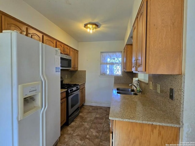 kitchen featuring light stone countertops, white fridge with ice dispenser, sink, range with gas cooktop, and decorative backsplash