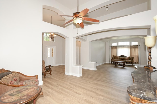 sitting room with a towering ceiling, light hardwood / wood-style floors, and ceiling fan with notable chandelier