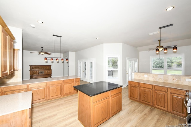 kitchen featuring stove, decorative backsplash, a kitchen island, decorative light fixtures, and light hardwood / wood-style floors