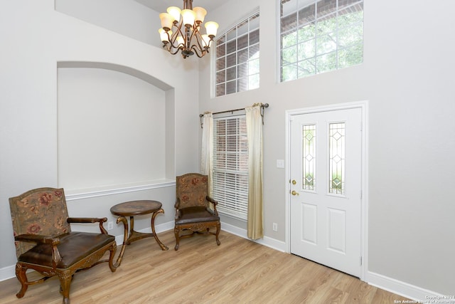 foyer featuring a towering ceiling, a healthy amount of sunlight, light wood-type flooring, and a notable chandelier