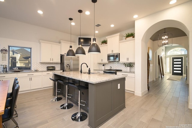 kitchen featuring sink, stainless steel appliances, an island with sink, decorative light fixtures, and white cabinets