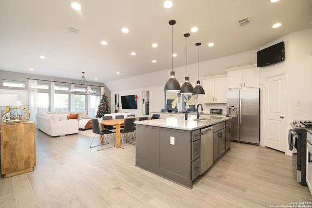 kitchen with appliances with stainless steel finishes, light stone counters, pendant lighting, a center island with sink, and white cabinets