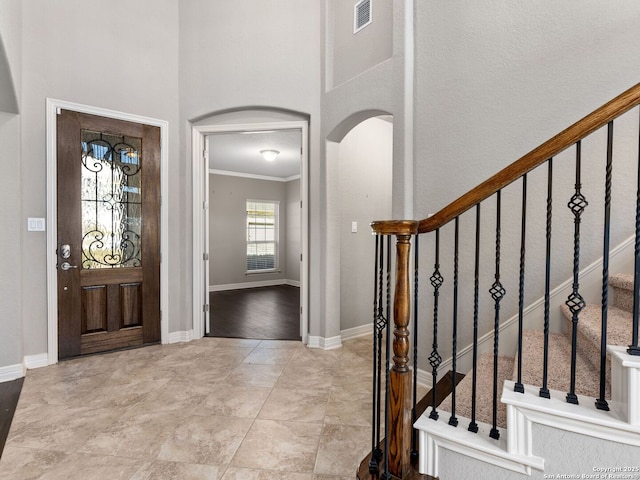 entryway with arched walkways, visible vents, ornamental molding, baseboards, and stairs