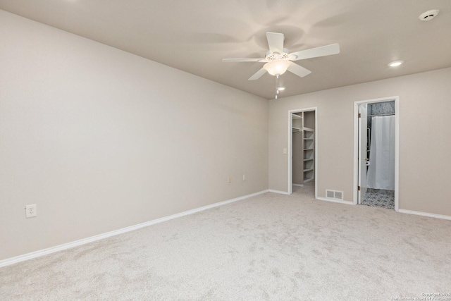 unfurnished bedroom featuring a spacious closet, ensuite bathroom, a closet, light colored carpet, and ceiling fan