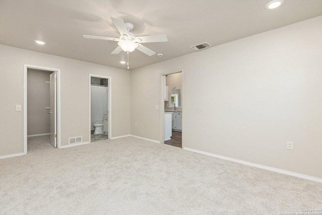 unfurnished bedroom with ensuite bath, light colored carpet, a walk in closet, and ceiling fan