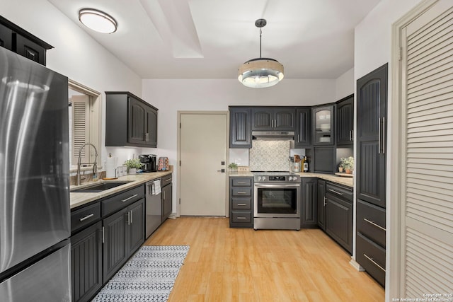 kitchen featuring backsplash, sink, hanging light fixtures, light wood-type flooring, and stainless steel appliances