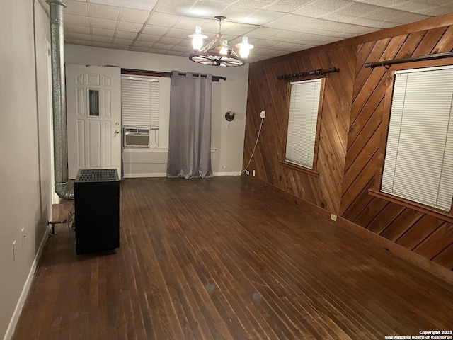 empty room featuring wooden walls, dark hardwood / wood-style flooring, cooling unit, and a notable chandelier