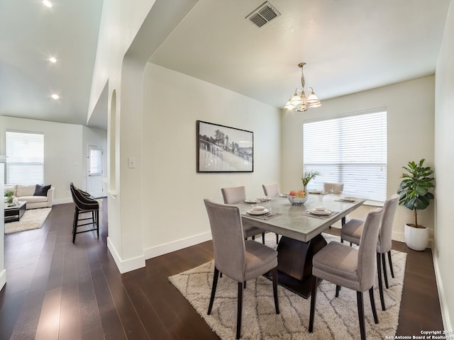 dining area with dark hardwood / wood-style floors, vaulted ceiling, and an inviting chandelier