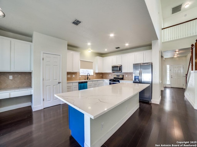 kitchen with light stone counters, stainless steel appliances, sink, a center island, and white cabinetry