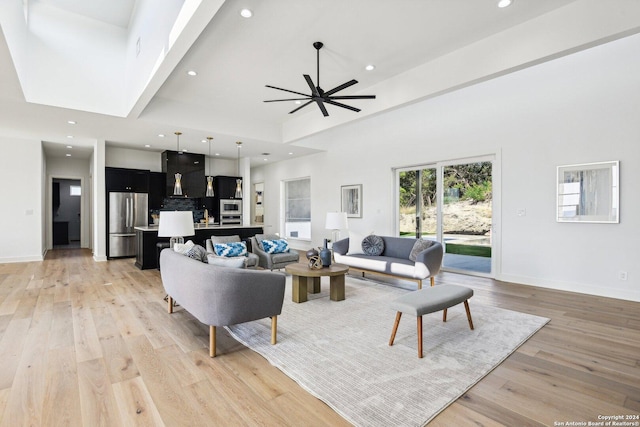 living room featuring ceiling fan, light hardwood / wood-style flooring, and a high ceiling