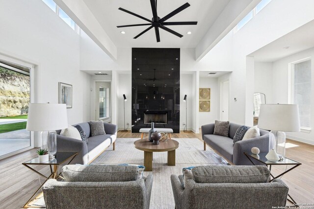 living room featuring a tiled fireplace, ceiling fan, light hardwood / wood-style flooring, and a high ceiling