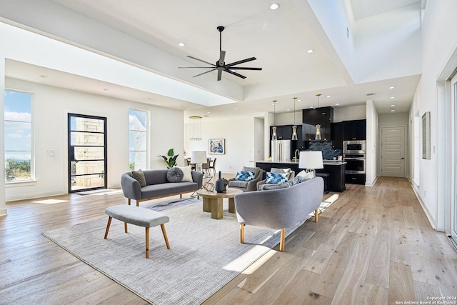 living room with ceiling fan, a high ceiling, and light hardwood / wood-style flooring