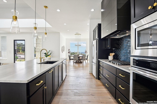 kitchen featuring tasteful backsplash, wall chimney range hood, sink, a large island with sink, and decorative light fixtures