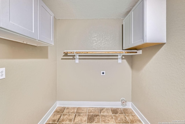 clothes washing area with hookup for an electric dryer, light tile patterned flooring, cabinets, and a textured ceiling