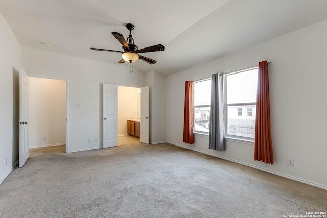 unfurnished bedroom with ensuite bath, ceiling fan, light colored carpet, and vaulted ceiling