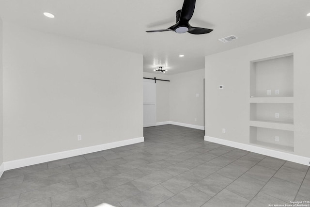 unfurnished room with a barn door, ceiling fan, and built in shelves