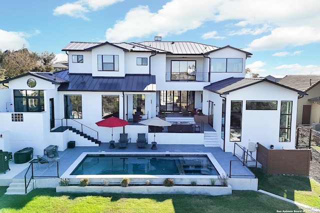 back of property featuring a yard, a swimming pool with hot tub, a balcony, and a patio