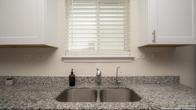 kitchen with white cabinets, light stone counters, and sink