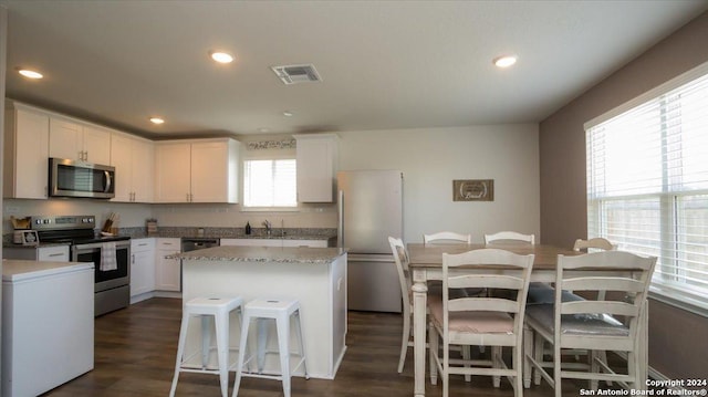 kitchen featuring stainless steel appliances, a kitchen island, dark hardwood / wood-style floors, a breakfast bar area, and white cabinets