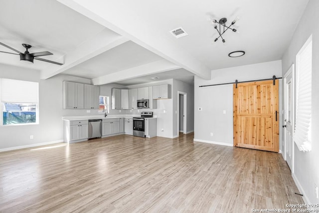 unfurnished living room featuring ceiling fan, sink, beam ceiling, a barn door, and light hardwood / wood-style floors