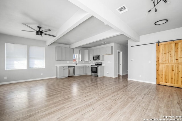 unfurnished living room featuring beam ceiling, a barn door, ceiling fan, and light hardwood / wood-style floors