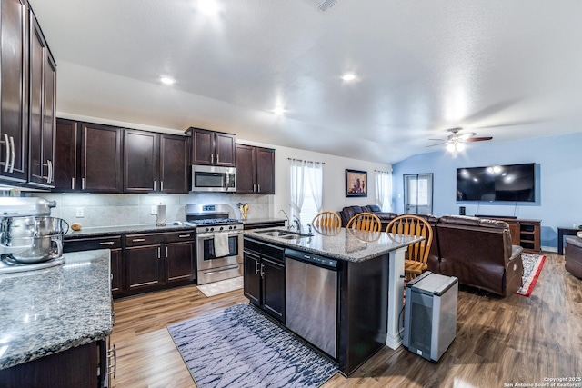 kitchen with lofted ceiling, backsplash, a center island with sink, a kitchen breakfast bar, and stainless steel appliances