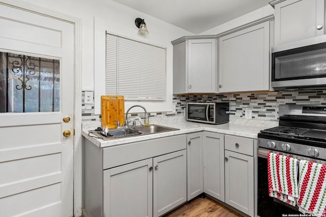 kitchen with sink, stainless steel appliances, tasteful backsplash, wood-type flooring, and gray cabinets