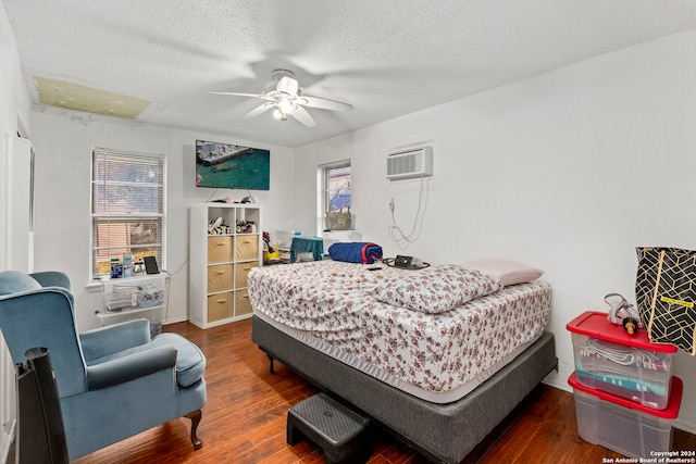 bedroom with a wall mounted air conditioner, ceiling fan, dark hardwood / wood-style floors, and a textured ceiling