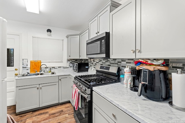 kitchen featuring sink, stainless steel appliances, light stone counters, backsplash, and light hardwood / wood-style floors