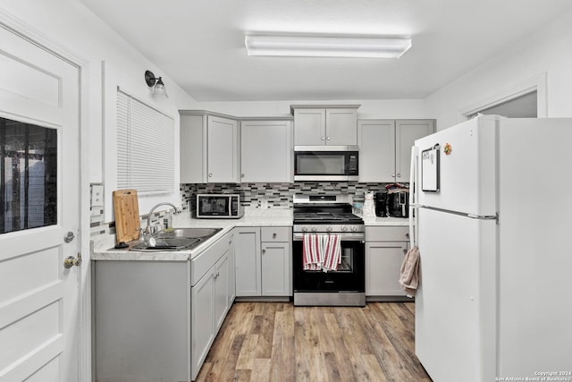 kitchen with gray cabinetry, backsplash, sink, light hardwood / wood-style flooring, and appliances with stainless steel finishes