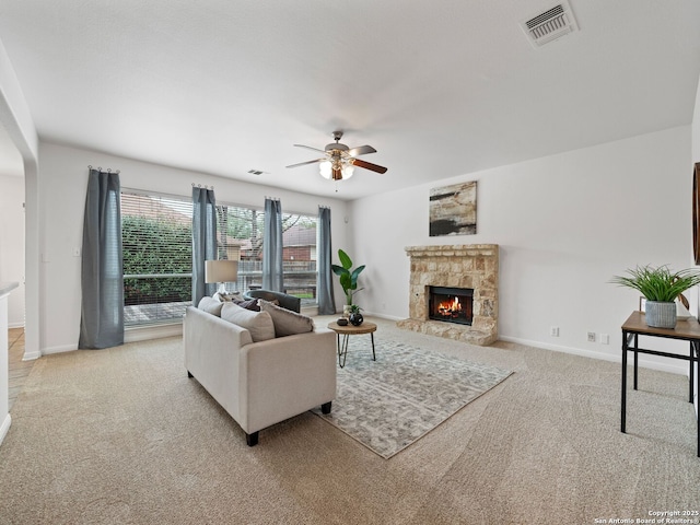 living area with ceiling fan, a stone fireplace, light colored carpet, visible vents, and baseboards